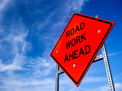 Bright orange sign that says Road Work Ahead
