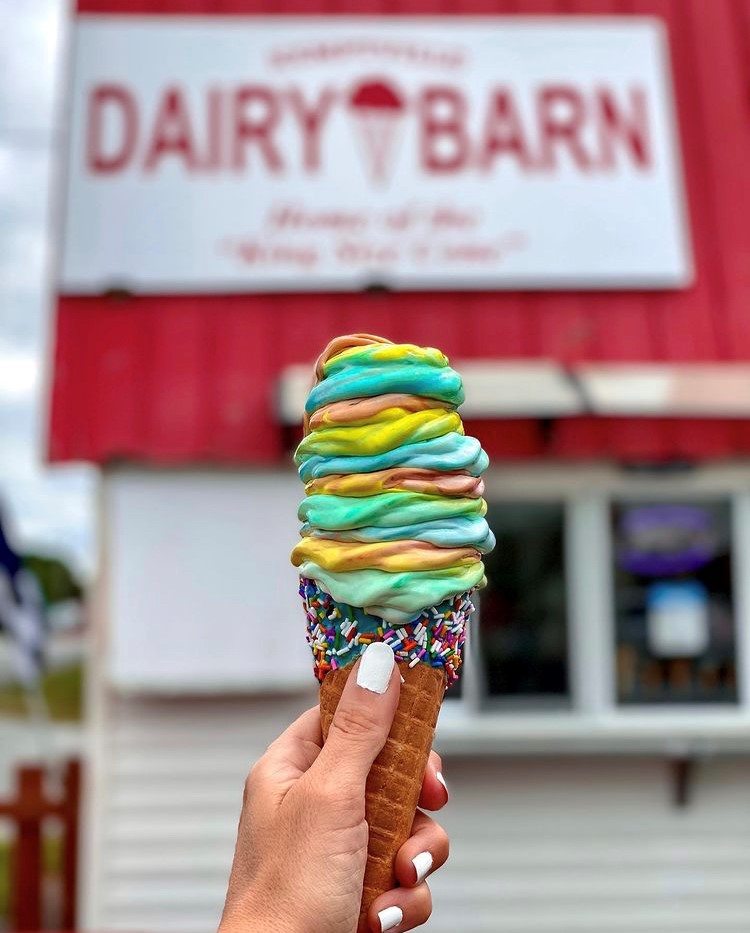 POV of person holding an colourful ice cream cone in front of the store sign for Kemptville Dairy Barn & Western Keto Grill.