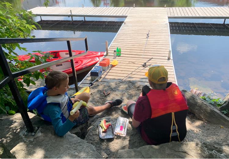 Father and son sit on a creek deck, setting up their fishing rods