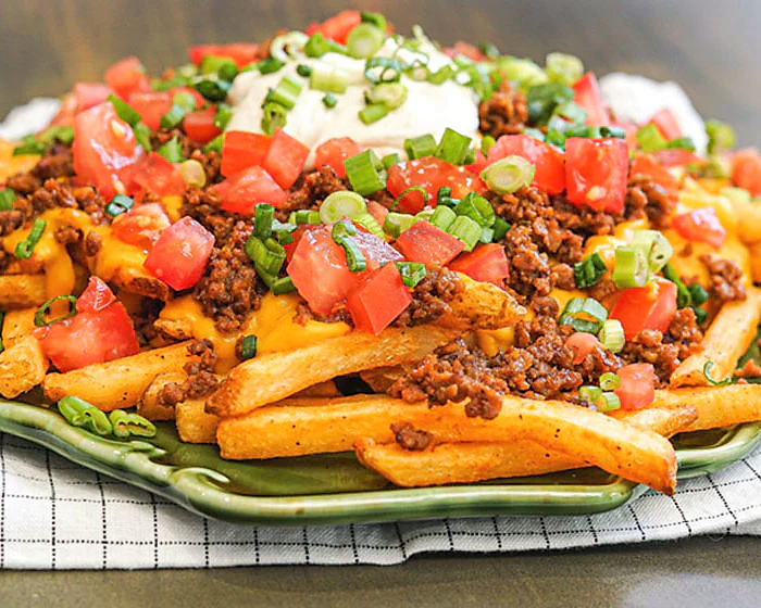 Plate of keto turnip fries topped with ground beef, cheese curds, tomatoes, sour cream, and green onions.