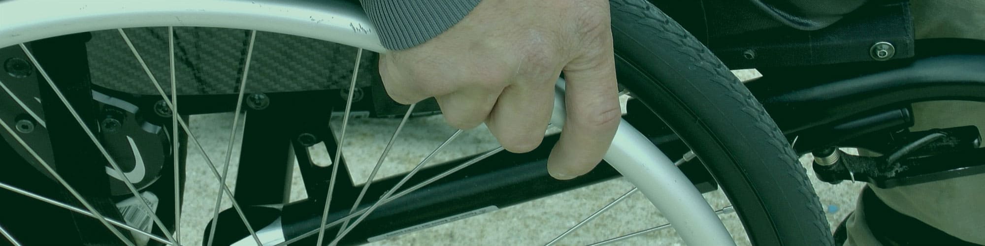A close-up of a hand holding a wheelchair wheel.