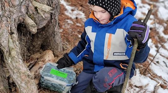 boy finds a geocache at the base of a tree 