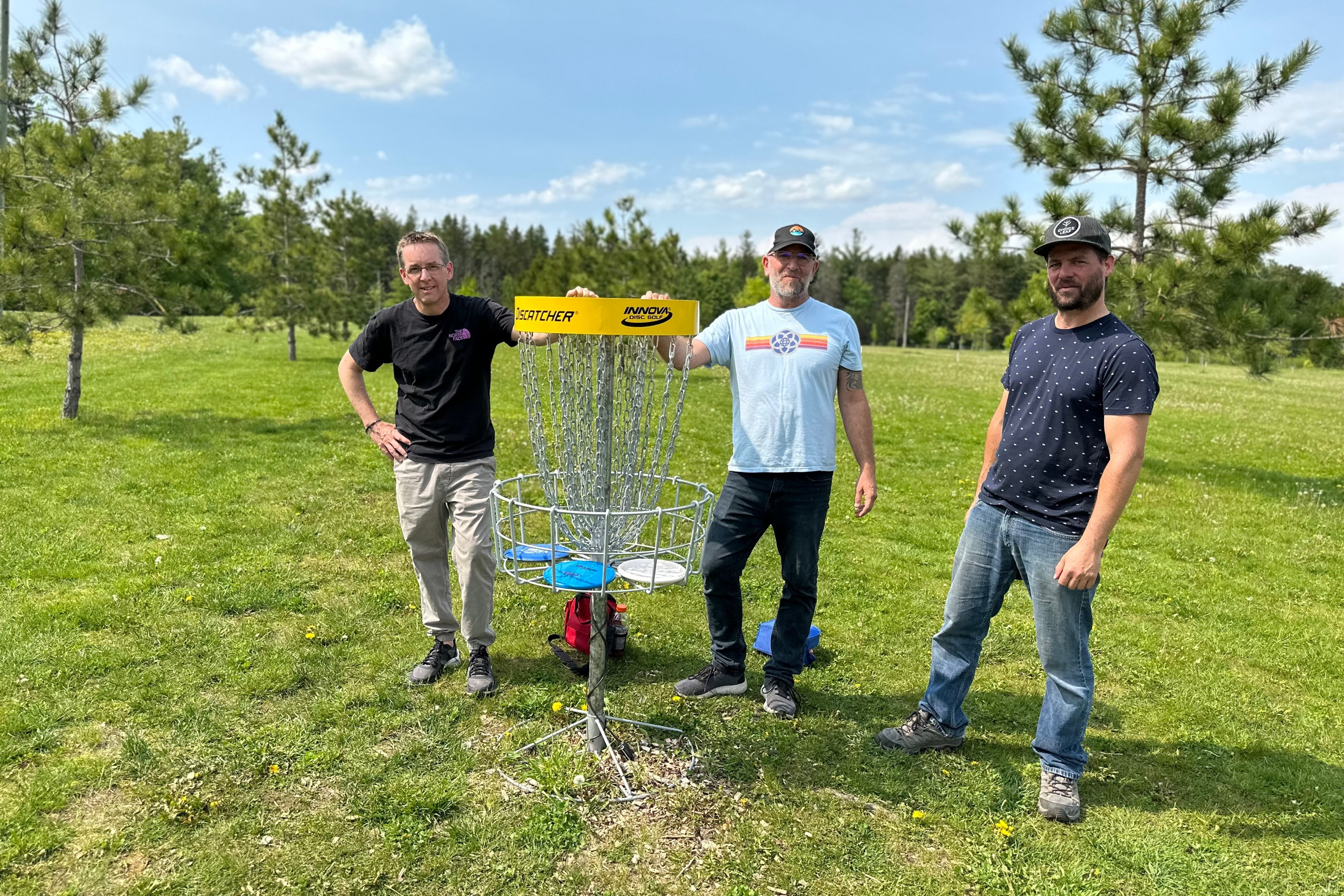 three men pose in front of a disc golf net