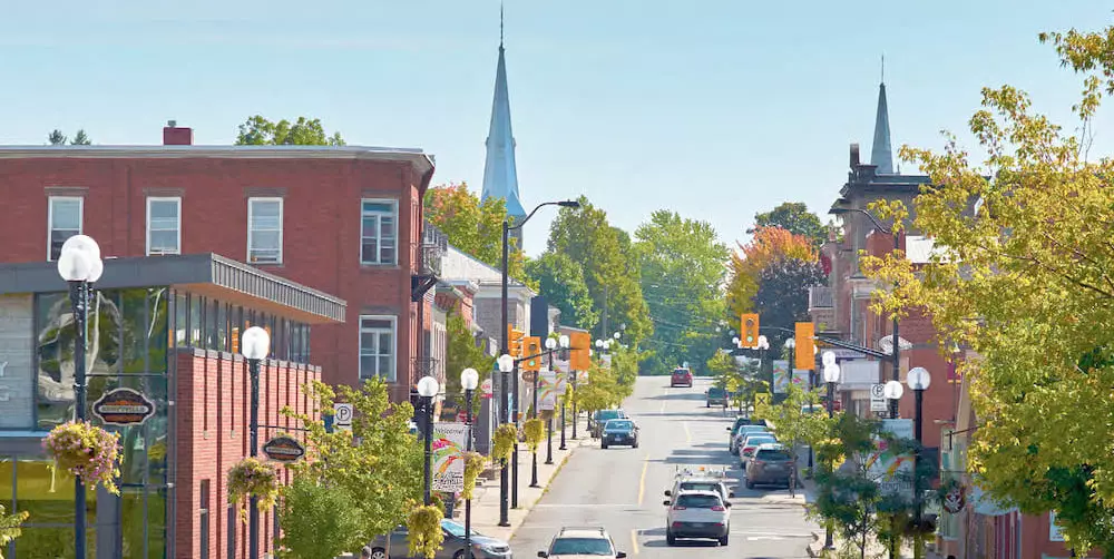 Long distance shot of downtown Kemptville's main road, featuring the library, church building, and cars traveling.
